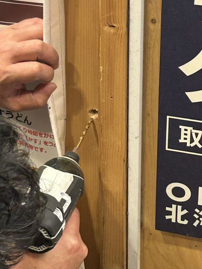 キューブの電源確保のためにお店のドアに穴を空けている作業